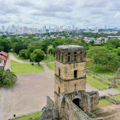 Vue aérienne des ruines de Panamá la Vieja, avec une tour en pierre partiellement détruite, et la skyline moderne de Panama City avec ses gratte-ciel en arrière plan.